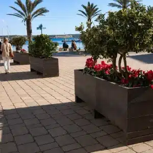 Detalle de la población Fornells donde vemos en segundo plano a una pareja caminando por el puerto y en primer plano a jardinera de plástico reciclado