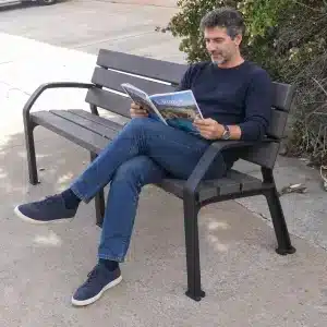 Vemos un banco ecológico de plástico reciclado y en él un hombre leyendo una revista de viajes todo vestido de azul